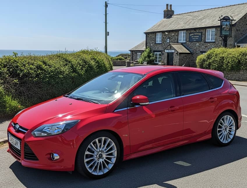 Blue Ford Focus on a Devon country lane with traditional stone walls and rolling hills, representing quality vehicle hire in Totnes's beautiful countryside